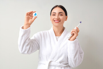 Beautiful young happy woman in bathrobe with dental floss and electric toothbrush on grey background