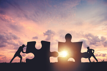 Silhouette of a team folding a puzzle against a sunset background, business and teamwork concept