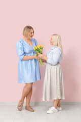 Adult woman with her mother and bouquet of tulips near pink wall. International Women's Day celebration