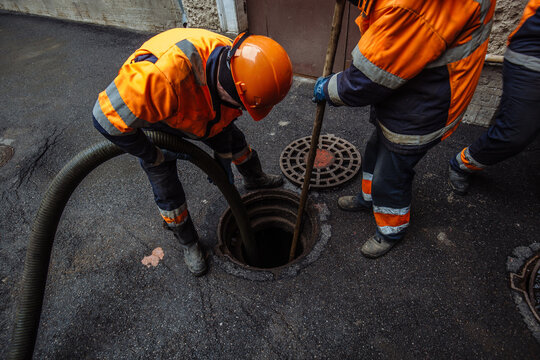 Sewer workers cleaning manhole and unblocking sewers the street sidewalk