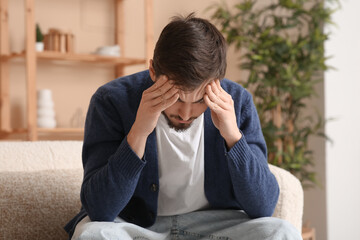 Tired young man with headache sitting on sofa at home