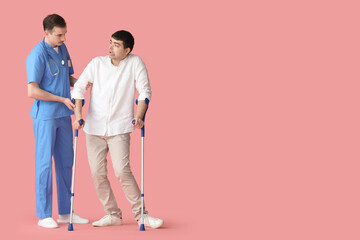 Young man with crutches and doctor on pink background. National Cerebral Palsy Awareness Month