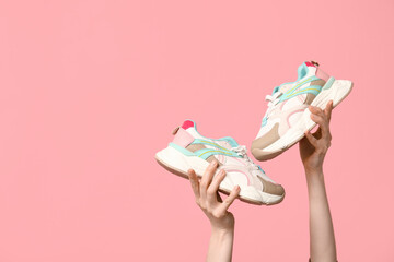 Female hands with stylish sneakers on pink background