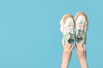 Female hands with stylish sneakers on blue background