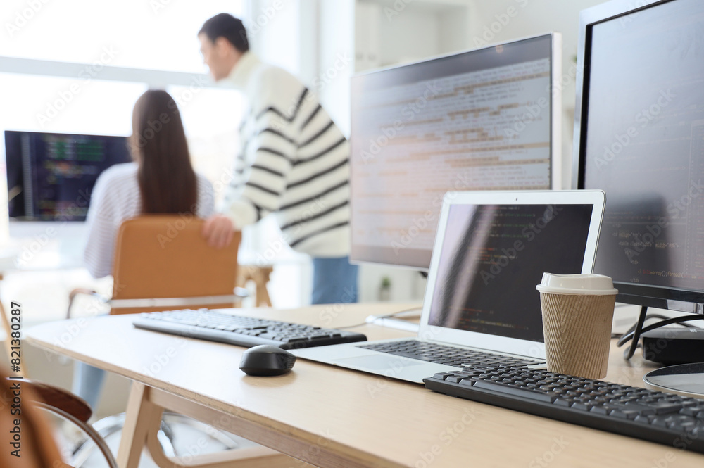 Poster computer monitors with laptop and coffee cup on programmer's table in office, closeup