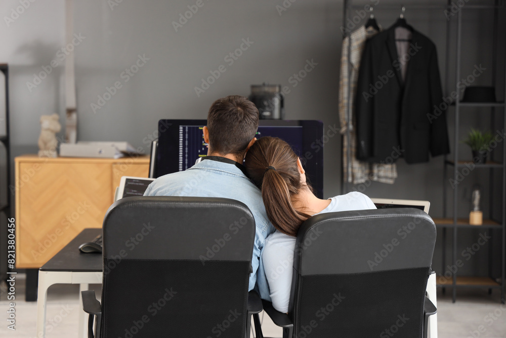 Poster young couple of programmers working at table in office, back view