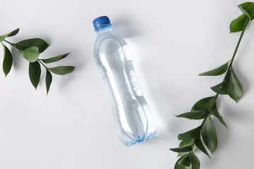 Bottle of clean water and leaves on white background