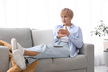 Upset mature deaf mute woman video chatting in sign language on sofa at home