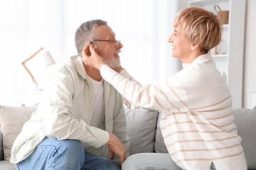 Mature woman putting hearing aid on her husband at home