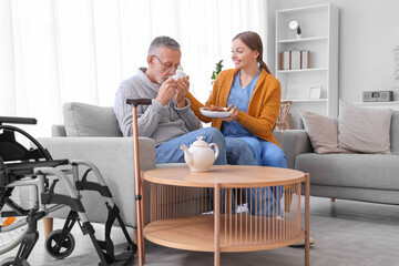 Senior man drinking tea with cookies and caregiver in nursing home