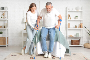 Nurse helping senior man with crutches in bedroom