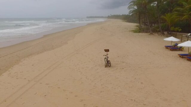 Drone mostrando bicicleta e praia semi deserta no litoral do nordeste brasileiro. V&iacute;deo a&eacute;reo de ondas quebrando no mar com vegeta&ccedil;&atilde;o tropical em praia paradis&iacute;aca