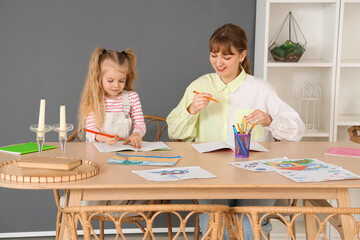 Nanny with cute little girl drawing on table at home