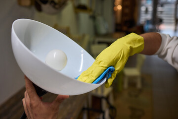 Person in yellow gloves cleans white bowl with blue cloth