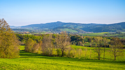 Obraz premium A breathtaking view of the Jested Ridge horizon, captured from a lush green field under a clear blue sky. The serene atmosphere suggests early morning or late afternoon. Located in Czech Republic