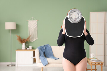Young overweight woman with weight scales at home
