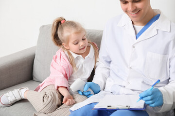 Fototapeta premium Male pediatrician measuring temperature of little girl with infrared thermometer in clinic