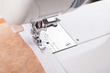 Modern sewing machine special presser foot with beige fabric and thread, closeup. Sewing process of sewing on a zipper. Business, hobby, handmade, zero waste, recycling, repair concept.