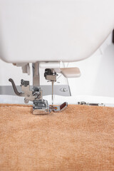 Modern sewing machine special presser foot with beige fabric and thread, closeup. Sewing process of...