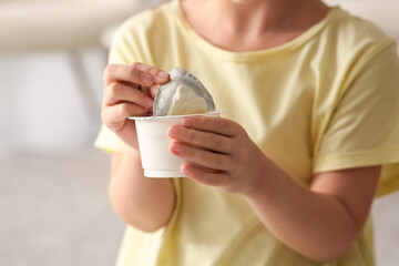 Cute little girl opening yogurt pack at home, closeup