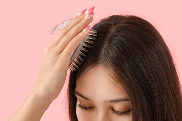 Young Asian woman brushing hair on pink background, closeup