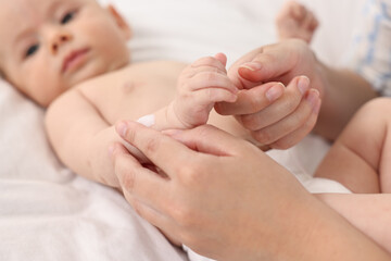 Woman applying body cream onto baby`s skin on bed, closeup