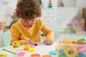 Cute little boy modeling from plasticine at white table in kindergarten. Space for text