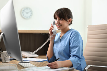 Smiling medical assistant talking by phone in office