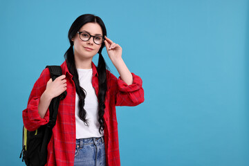 Student in glasses with backpack on light blue background. Space for text
