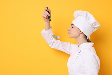 Professional chef with ladle tasting something on yellow background. Space for text