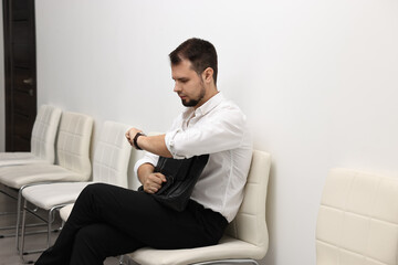Man looking at wrist watch and waiting for job interview indoors