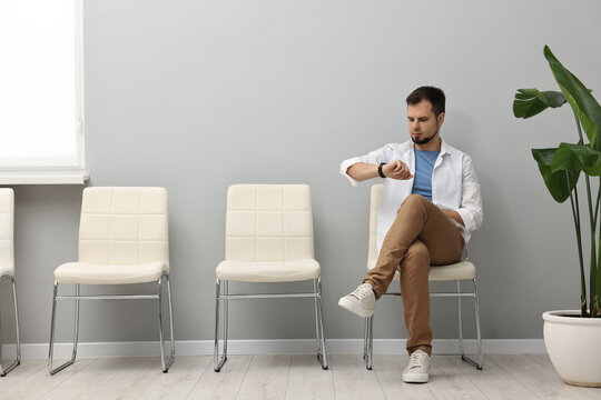 Man looking at wrist watch and waiting for appointment indoors