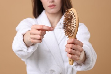 Woman taking her lost hair from brush on light brown background, closeup. Alopecia problem