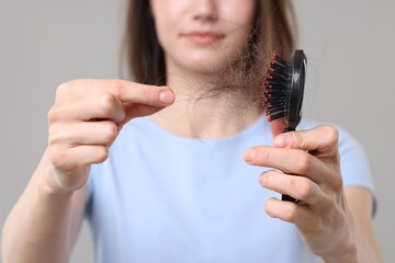 Woman taking her lost hair from brush on grey background, closeup. Alopecia problem