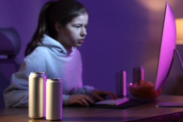Girl playing computer game at home, focus on cans with energy drink