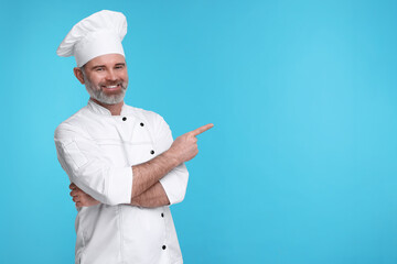 Happy chef in uniform pointing at something on light blue background, space for text