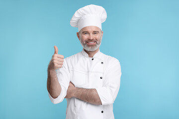 Happy chef in uniform showing thumbs up on light blue background