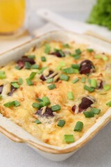 Tasty sausage casserole with green onions in baking dish on white table, closeup