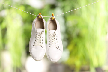 Stylish sneakers drying on washing line against blurred background