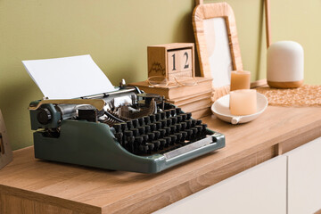 Vintage typewriter with books on commode near green wall, closeup