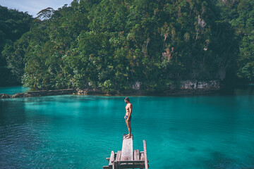 Vacation and activity. Young man enjoying blue tropical lagoon view standing on wooden springboard....