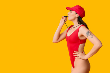 Female lifeguard blowing into whistle on yellow background