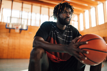 Portrait of african man basketball player holding ball while sitting on a bench