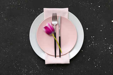 Beautiful table setting with plates,  cutlery, napkin and flower on black background