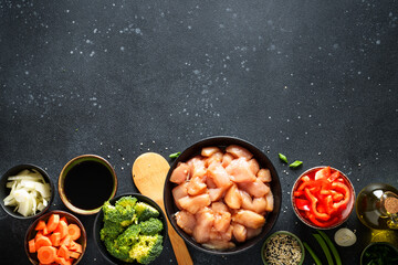 Chicken stir fry with vegetables cooking ingredients at black background. Flat lay with copy space.