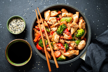 Chicken stir fry with soy sauce and vegetables at black background. Flat lay with copy space.