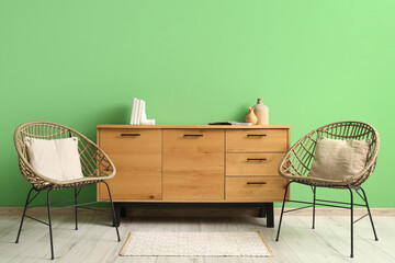 Armchairs and wooden chest of drawers near green wall in modern room