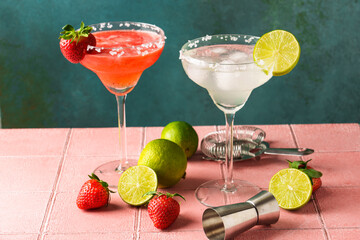 Classic and strawberry margarita in tall glasses with tequila, ice and lime at color background.