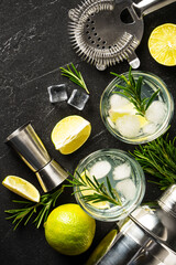 Gin tonic. Alcohol cocktail with gin, tonic, ice cubes, lime and rosemary on black background. Top...