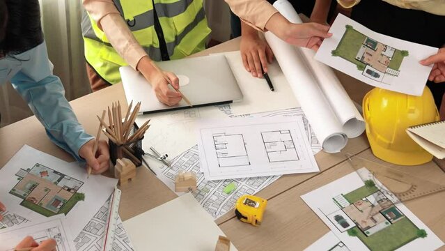 Smart architect and safety engineer discussion about building blueprint on table with architectural document, measurement tools and wooden block scatter around at modern office. Closeup. Delineation.